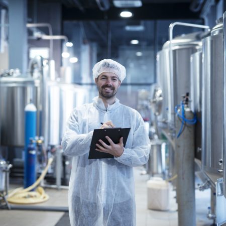 Food processing plant interior with positive smiling technologist holding checklist. ISO 22000:2018 – Food Safety Management System